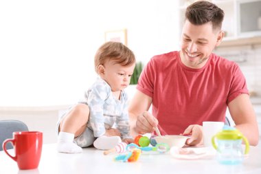 Baba küçük oğlunu mutfakta besliyor.