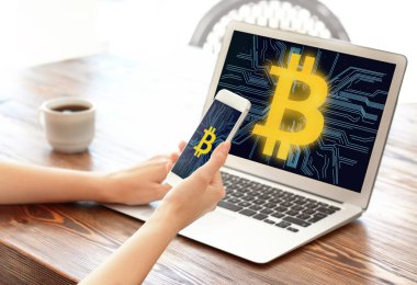 Masada ekranlarda bitcoin sembolleri ile dizüstü bilgisayar ve akıllı telefon kullanan kadın