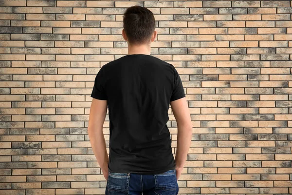 年轻男子穿着时髦的 T恤衫 在砖墙背景 设计样机 — 图库照片