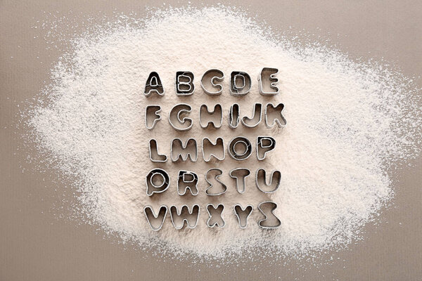 Cookie cutters in shape of alphabet letters on scattered flour