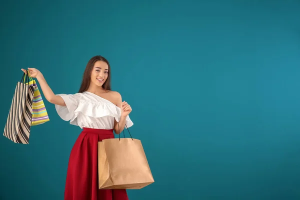 Beautiful young woman with shopping bags on color background