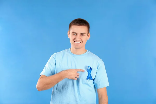 Joven apuntando a la cinta azul en su camiseta contra el fondo de color. Concepto de conciencia del cáncer de próstata — Foto de Stock