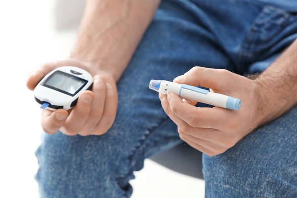 Diabetic man holding digital glucometer and lancet pen, closeup