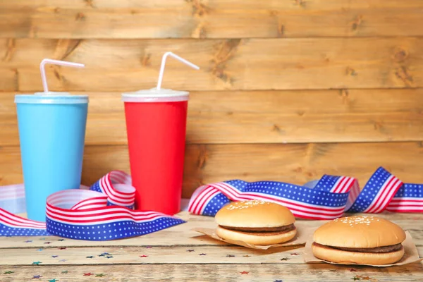 美味的汉堡包 美国国旗丝带和杯子在木桌上的饮料 — 图库照片