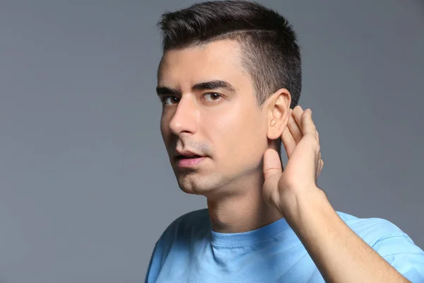 Молодий чоловік з проблемою слуху на сірому фоні — стокове фото