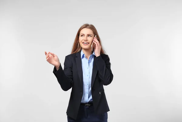 Mooie jonge vrouw in elegante pak praten via de mobiele telefoon op lichte achtergrond — Stockfoto