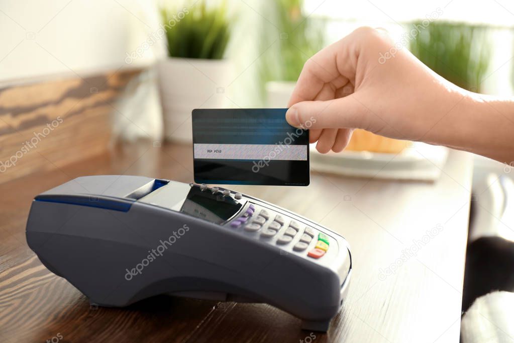 Woman using bank terminal for credit card payment on wooden table