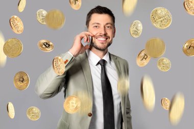 Telefon ve gri arka plan üzerinde düşen bitcoins konuşurken mutlu işadamı