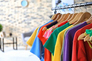 Rack with rainbow clothes on hangers indoors clipart