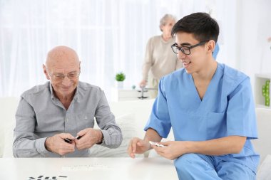 Senior man playing dominoes with young caregiver at home