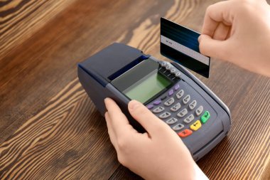 Ahşap masa üzerinde kredi kartı ödeme banka terminal kullanan kadın