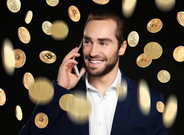 Telefon ve siyah arka plan üzerinde düşen bitcoins konuşurken mutlu işadamı