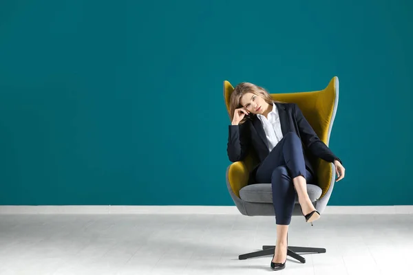 Mulher elegante bonita em terno elegante sentado em poltrona contra parede de cor — Fotografia de Stock