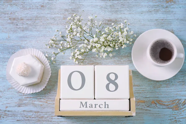 Wooden block calendar, flowers, dessert and cup of coffee on table. International Women's Day celebration