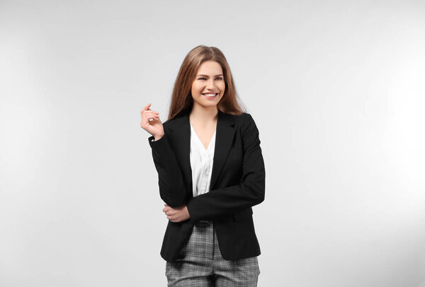 Beautiful young woman in elegant suit on light background