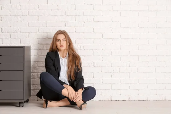 Mulher elegante bonita em terno elegante sentado no chão contra a parede de tijolo branco — Fotografia de Stock