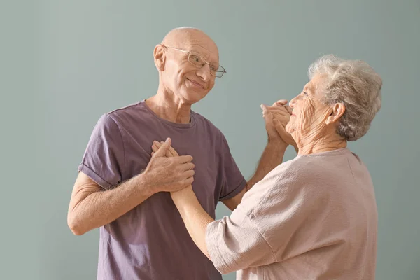 Cute elderly couple dancing against color background