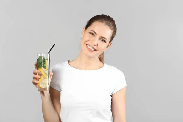 Hermosa joven con vaso de limonada sobre fondo gris — Foto de Stock