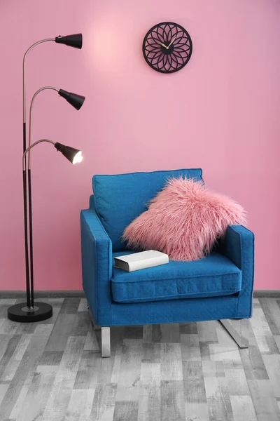 Armchair with fluffy pillow near color wall