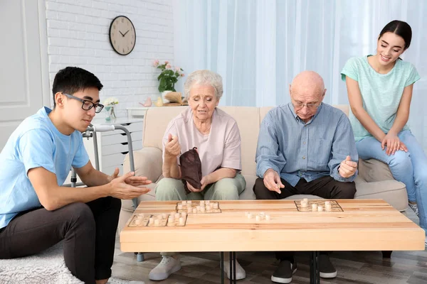 Personas mayores jugando bingo con jóvenes cuidadores en casa — Foto de Stock