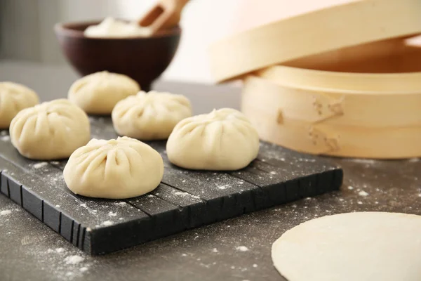 Tablero de madera con albóndigas de baozi crudas en la mesa — Foto de Stock