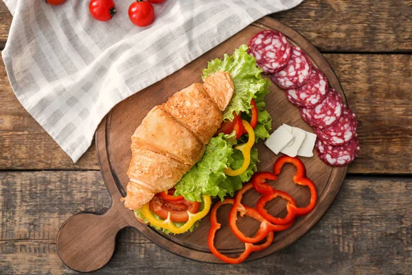 Placa de madeira com delicioso sanduíche de croissant na mesa — Fotografia de Stock