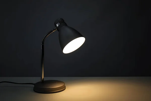 Stylish desk lamp on table in darkness — Stock Photo, Image