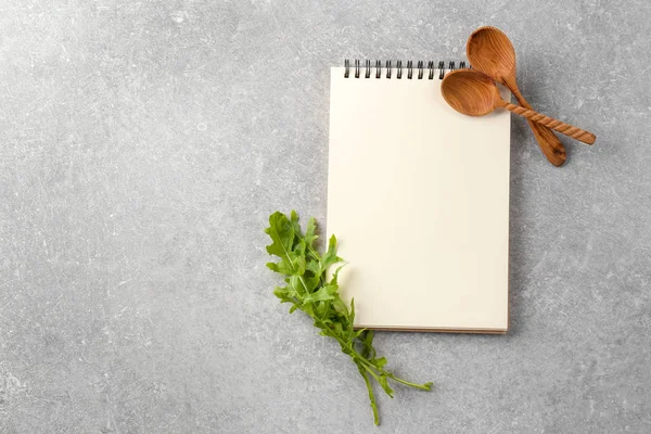 Notizbuch mit Kochlöffeln und Rucola auf grauem Hintergrund. Kochmeisterkurse — Stockfoto