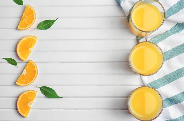 Vasos con zumo de naranja fresco y fruta sobre mesa de madera — Foto de Stock