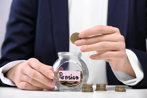 Woman putting coin into glass jar with label "PENSION" on table — Stock Photo, Image