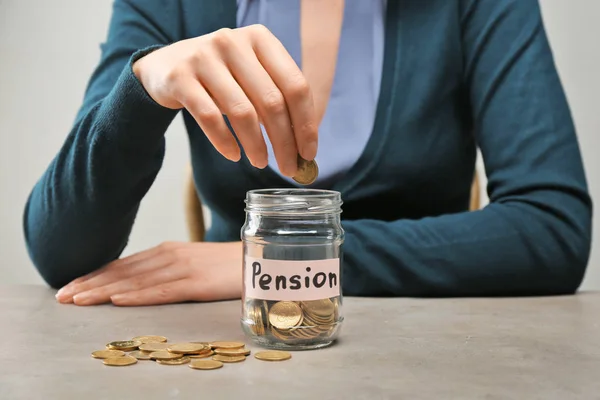 Kvinde sætte mønt i glas krukke med etiketten "PENSION" på bordet - Stock-foto