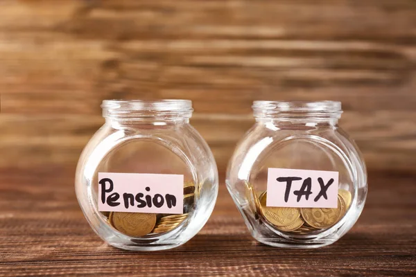 玻璃罐子与标签 "退休金", "税" 和硬币在木桌 — 图库照片
