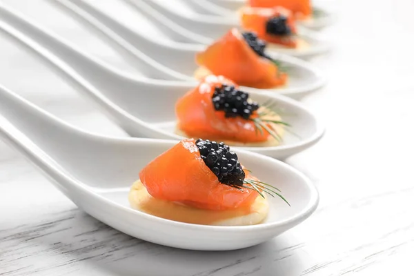 Aperitivos saborosos com caviar preto e salmão em colheres de cerâmica na mesa — Fotografia de Stock