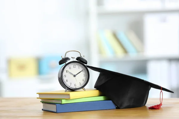 Alarm clock, graduation cap and textbooks on table. Study goals