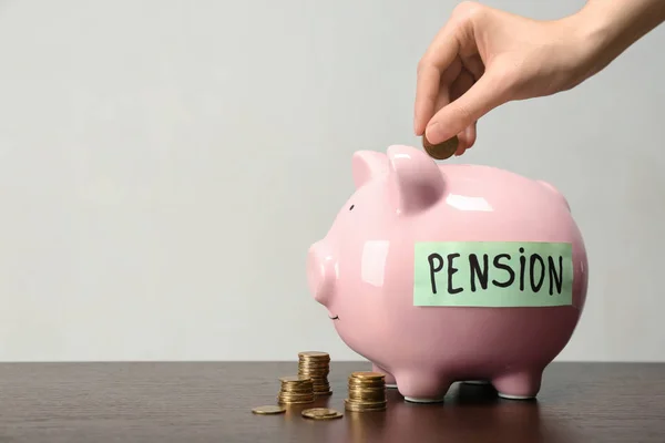 Woman putting coin into piggy bank with label "PENSION" at table — Stock Photo, Image