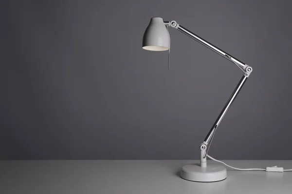 Stylish desk lamp on table against gray background