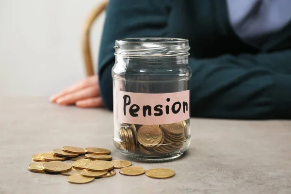 Monedas en frasco de vidrio con etiqueta "PENSIÓN" y mujer borrosa en el fondo — Foto de Stock