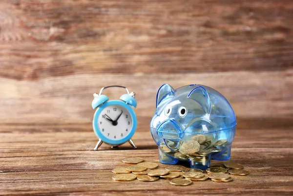 Piggy bank with coins and alarm clock on wooden table. Pension planning