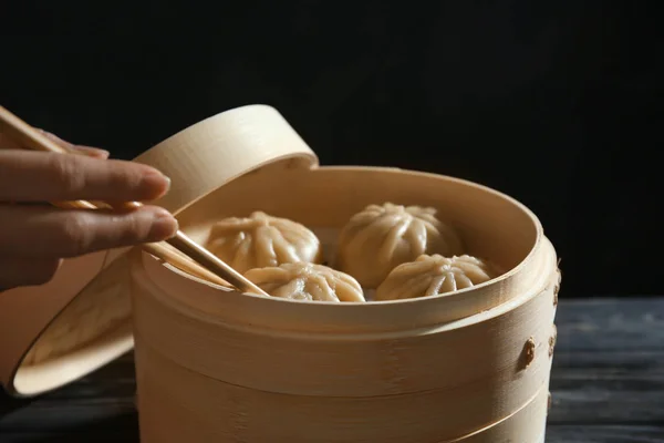 Mujer sosteniendo albóndigas baozi con palillos cerca de vapor de bambú, primer plano — Foto de Stock