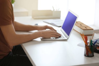 Genç adam ofiste dizüstü bilgisayarla çalışıyor.