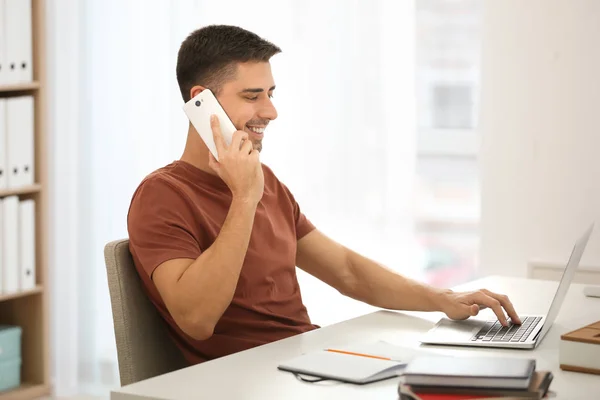 A fiatalember beszél telefonon laptop az irodai munka közben — Stock Fotó