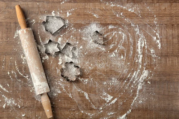 Farinha espalhada, rolo e cortadores de biscoitos na mesa de madeira — Fotografia de Stock