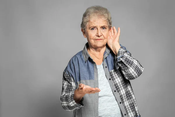 Elderly woman with hearing problem on grey background