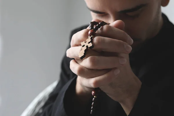 Joven sacerdote orante con cuentas de rosario sobre fondo claro, primer plano — Foto de Stock