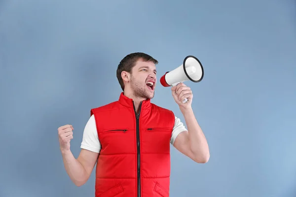 Knappe man in rode vest schreeuwen in Megafoon op kleur achtergrond — Stockfoto