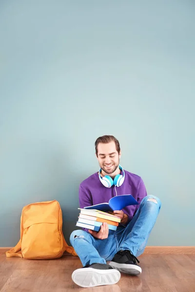 Studente con quaderni seduto sul pavimento contro la parete a colori — Foto Stock