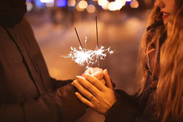 Young loving couple holding sparklers outdoors on winter evening — Stock Photo, Image