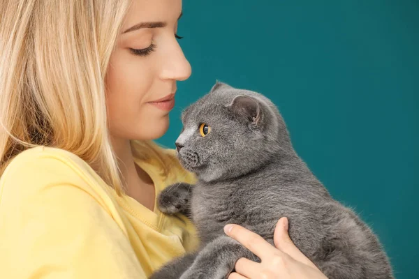 Mujer joven con lindo gato mascota en el fondo de color — Foto de Stock