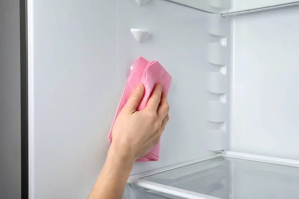 Woman cleaning refrigerator with rag, closeup