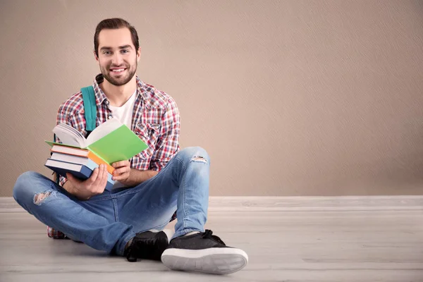 Studente con quaderni seduto sul pavimento contro la parete a colori — Foto Stock